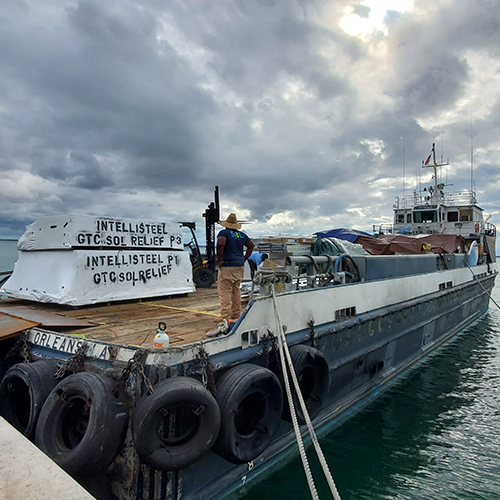 Man unloading boat loaded with the prefabricated frames of several houses shipped during disaster recovery efforts.