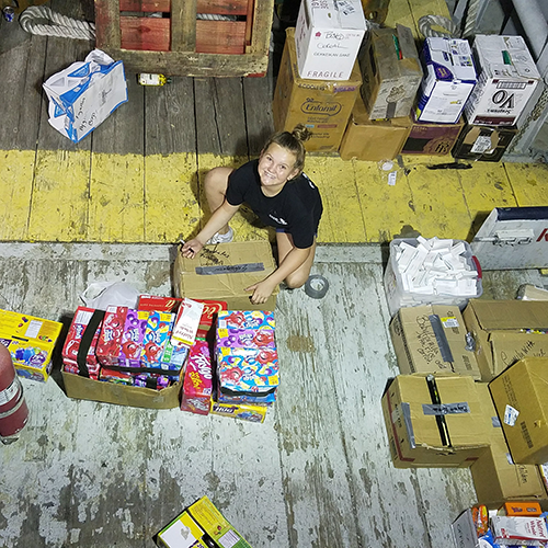 Young lady sorting donations of food, medicine, diapers, etc. on the back of a boat for distribution at night.