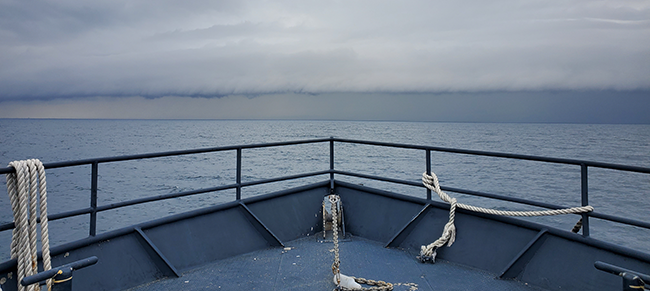 Bow of a boat heading into a large storm on the horizon on the ocean.