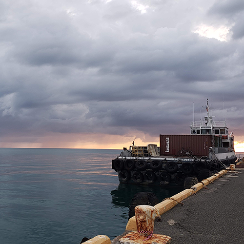 Shipping boat tied up to bulkhead at sunset with a storm on the horizon.