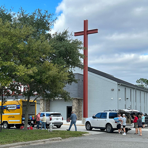 Large cross outside of a church while church members load donations into a moving van.