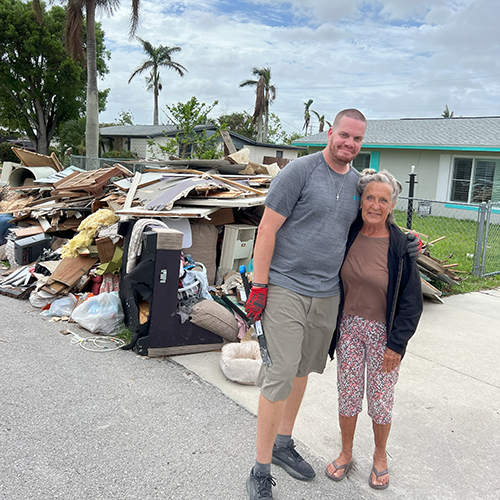 Volunteer stands with homeowner in front of her home that flooded during hurricane.