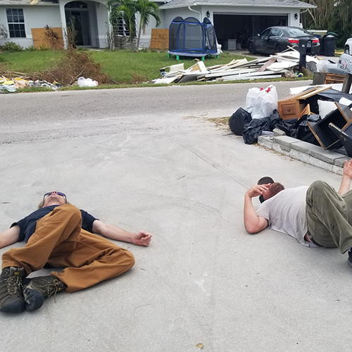 Two men lay in a driveway after a long day of hurricane clean up and debris removal.