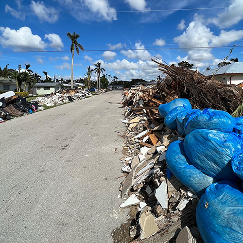 Debris down a road where every home flooded under a beautiful sunny sky.