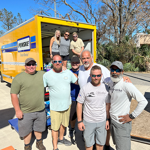 Volunteers stand together after unloading large moving van full of donations for hurricane relief support.