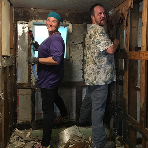 Volunteers have fun while gutting bathroom together in a flooded home.