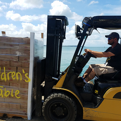 Man driving a forklift with a large pallet of donated food for disaster relief shipped by nonprofit shipping ministry.