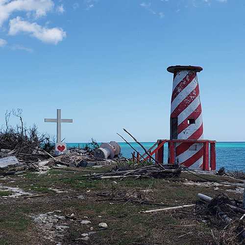 Broken red and white striped lighthouse and cross sitting above the ocean in High Rock after a hurricane.