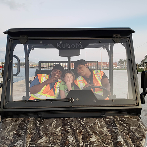 Little girl sits in a golf cart with two security guards in the port of Freeport.