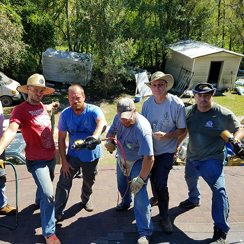 Team of volunteers pose with roofing tools.