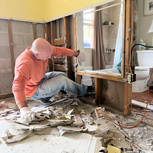 Volunteer kicks wet and moldy drywall out of the studs in a home that was flooded during a hurricane.