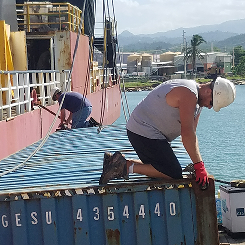 Captain and volunteer secure crane to shipping container to be unloaded from the boat in Puerto Rico during hurricane response mission.