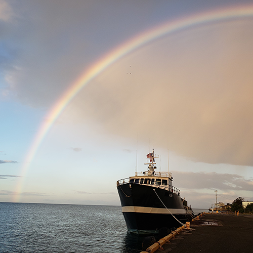 The Glory, a nonprofit shipping vessel at sunset under a rainbow after a storm in Puerto Rico.