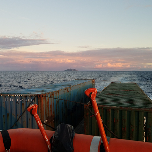 View from the back of a shipping boat with containers at sunset.