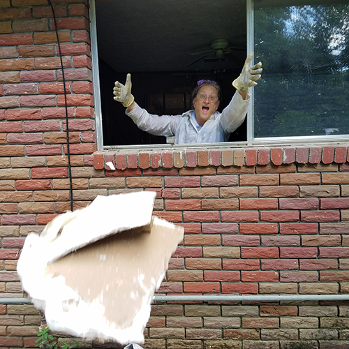 Volunteer dramatically throws drywall out a window.