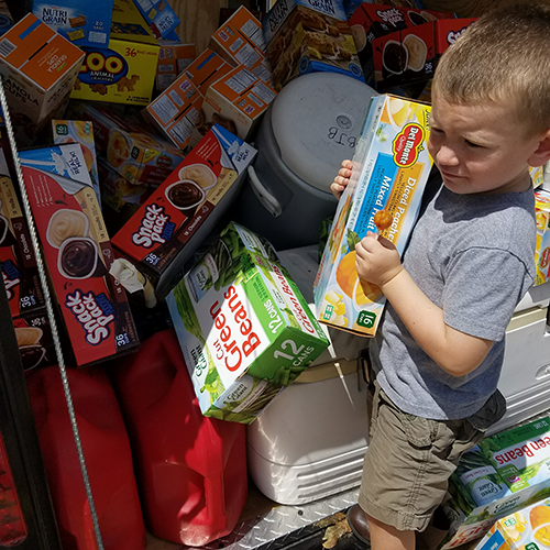 Little boy helps unload trailer of donated food for hurricane distribution center.