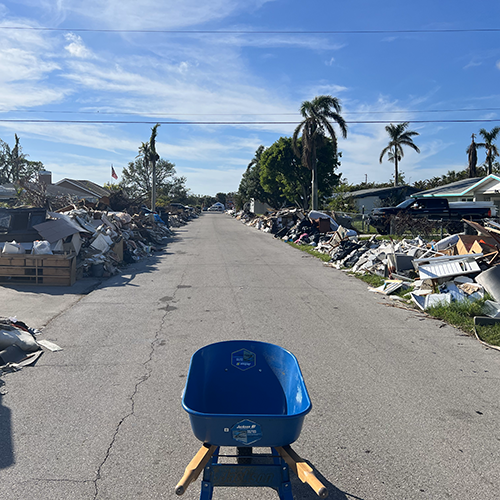 Blue wheelbarrow in the middle of a street lined with debris from flooding after hurricane.