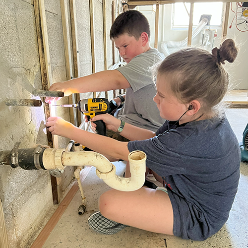 Children help replace furring strips in a home that had to be gutted after flooding.